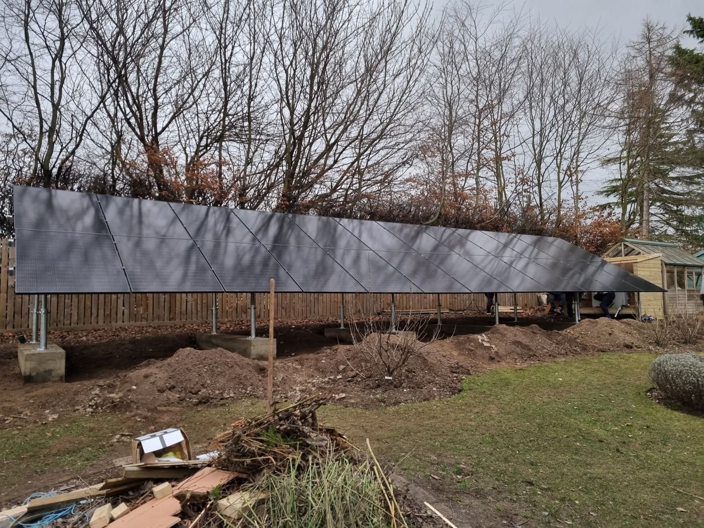 Solar panels on a ground-mount frame held up by posts set in concrete footings in a garden