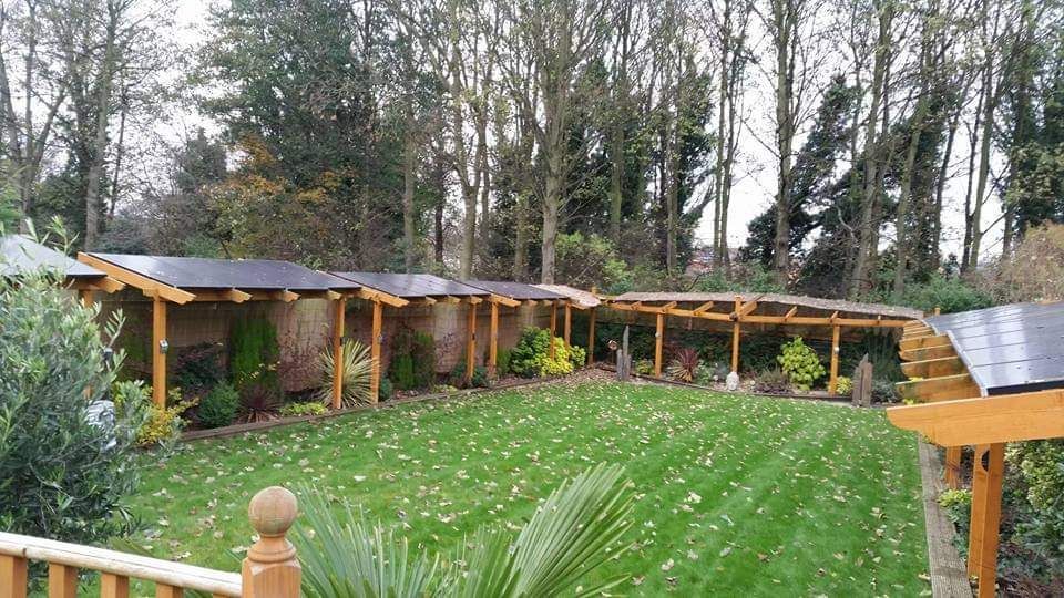 A long timber solar pergola running along the border of a large lawned garden