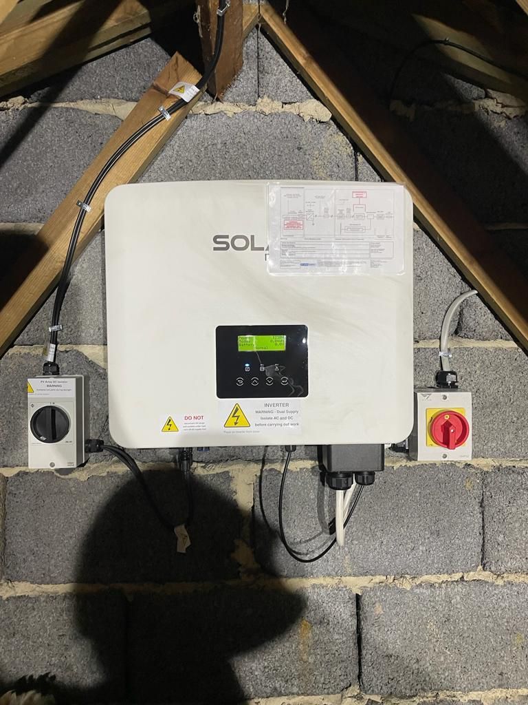 A SolaX inverter with isolator switches mounted on a block wall in a loft